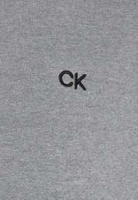 Grauer Baumwoll-Sweatshirt mit einem kleinen schwarzen gestickten "CK"-Logo auf der Brust, mit einer glatten, gleichmäßigen Textur.