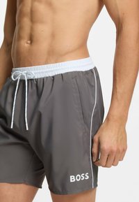 Heren zwemshorts in grijs, met een witte elastische tailleband met trekkoord, zijzakken en een wit logo linksonder.