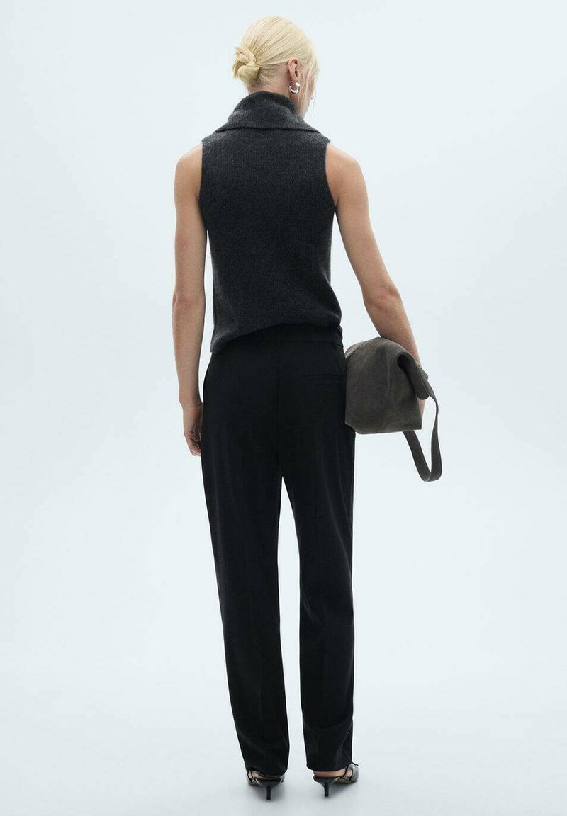 Szary bezrękawnik z wysokim kołnierzem, w połączeniu z czarnymi spodniami. W lewej ręce trzymana jest mała ciemna torba. Prosty, niezdobiony design.