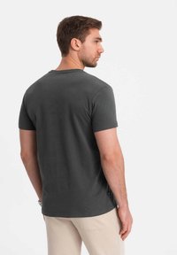 Grå, kortærmet t-shirt med rund hals og en glat tekstur, parret med lyse bukser. Har et logomærke på siden.