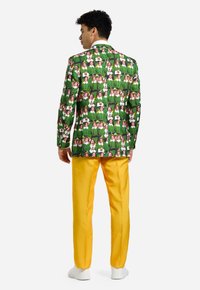 Zelený vzorovaný blazer s opakujúcimi sa obrázkami, skombinovaný s jasne žltými nohavicami. Blazer má klopový golier a štíhly strih.