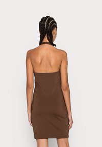 Vestido castanho sem alças, feito de um tecido suave, com um formato justo, costuras mínimas e uma barra que termina a meio do coxa. Laços no pescoço para suporte.