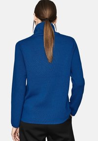 Maglione blu a costine con colletto alto e maniche lunghe, caratterizzato da una finitura testurizzata e da una vestibilità comoda. Pantaloni visibili in basso.