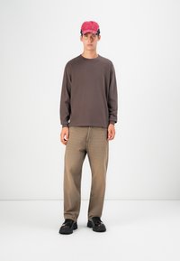 Cămașă lungă maro cu mânecă lungă, pantaloni largi de culoare maro deschis, pantofi masivi negri și o cinci panouri roz. Design simplu, casual, cu detalii minime.