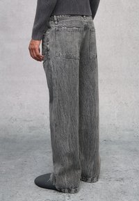Jeans gris de pierna ancha con una textura desgastada y costuras visibles, que cuentan con dobles bolsillos traseros, detalles envejecidos y un ajuste casual.