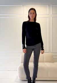 Juoda ilgomis rankovėmis palaidinė su mygtukų akcentais ant rankovių, derinama su tamsių tonų raštuotomis tampriomis kelnėmis ir aulinukais. Neutralus fonas.