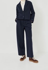 Costume à rayures marines avec blazer court et pantalon à jambes larges. Tissu mat, fermeture à un bouton. Baskets marron texturées avec lacets blancs.