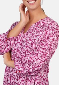 Floral-print dress in shades of pink and white, featuring a v-neckline, long puff sleeves, and red button accents on the cuffs.