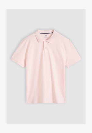 Vaaleanpunainen lyhythihainen poolopaita, jossa on kaulus ja kaksinappinen nappilista, asetettuna tasaisesti vaaleanharmaalla taustalla.