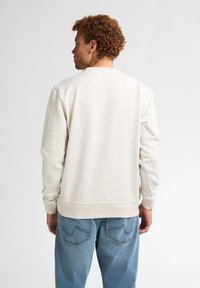 Felpa color crema con un motivo testurizzato, scollatura rotonda e polsini a costine. Abbinata a jeans di denim azzurro chiaro.