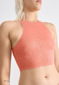 Koral sports-bh med et struktureret, mønstret design. Uden ærmer med en bølget kant, lavet af strækbart materiale for komfort.