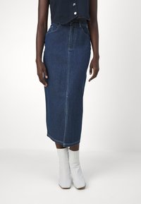 Tamsiai mėlyna džinsinė sijonas, iki kelių, tiesaus kirpimo, su diržo kilpomis ir priekiniu kišeniu. Derinamas su baltomis kulkšnies botąmis.