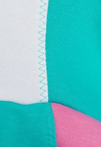 Gros plan de panneaux de tissu blancs, turquoise et roses avec des coutures en zigzag reliant les coutures dans un motif géométrique.