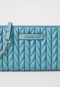 Quilted blue leather handbag with a silver chain strap, featuring a logo plate and a chevron pattern across the surface.