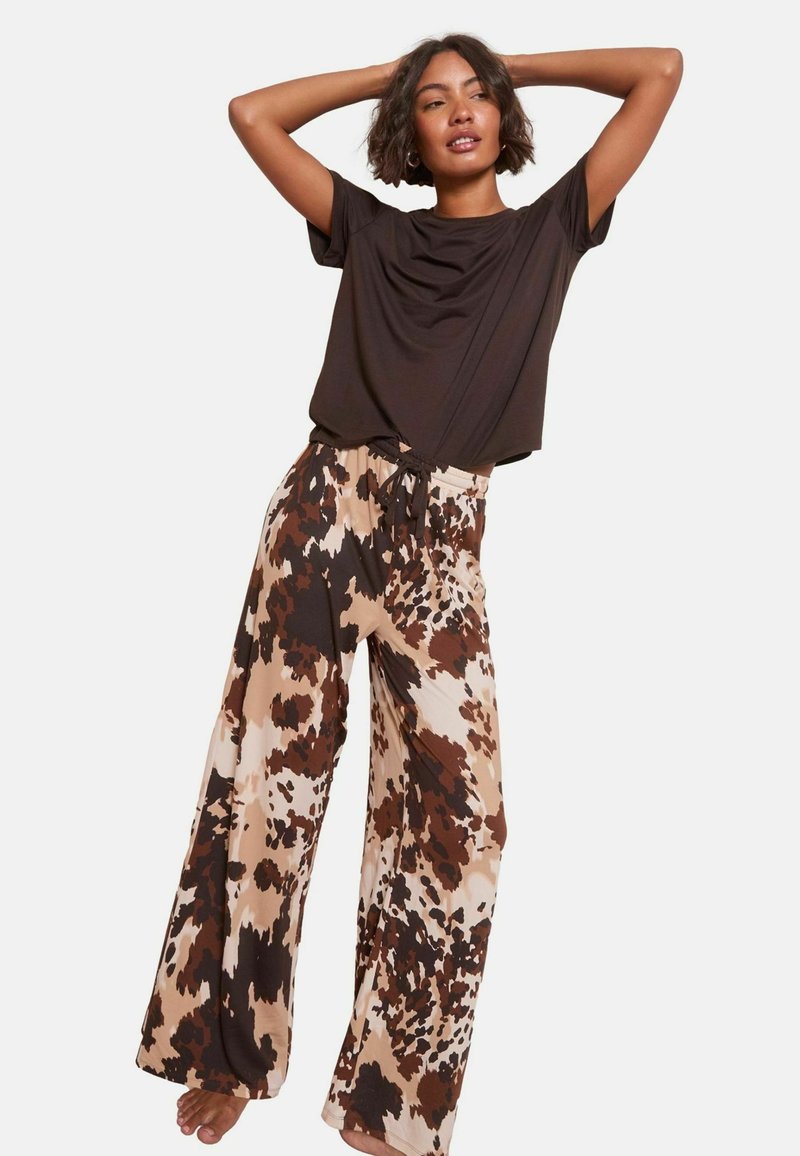 Top corto a maniche corte marrone abbinato a pantaloni a gamba larga con un motivo astratto marrone e beige. I pantaloni hanno una vita elasticizzata con un cordino.
