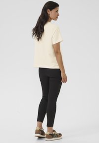 T-shirt crème à manches courtes avec une coupe décontractée, associé à un legging noir et des baskets décontractées avec des accents marron et beige.