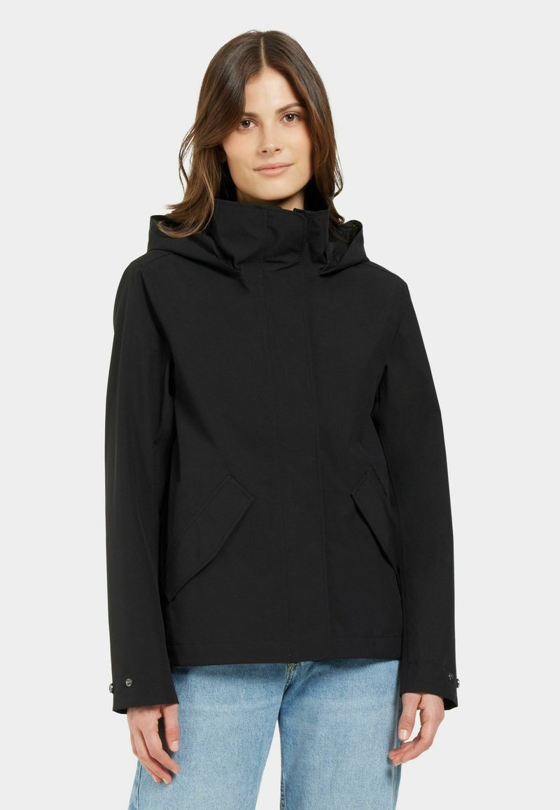 Musta vedenpitävä takki, jossa on korkea kaulus, etujenkki ja sivutaskut. Varustettu hupulla ja kestävästä kankaasta, joka on sileä kosketukseltaan.