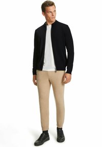 Marineblauer Reißverschlussjacke, weißem T-Shirt, beigefarbenen tapered Pants und schwarzen Sneakers; weicher Stoff mit lässiger Passform. Minimalistisches Design, keine Muster.