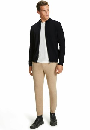 Veste zippée marine, t-shirt blanc, pantalon chino beige, et baskets noires ; texture douce avec une coupe décontractée. Design minimaliste, sans motifs.