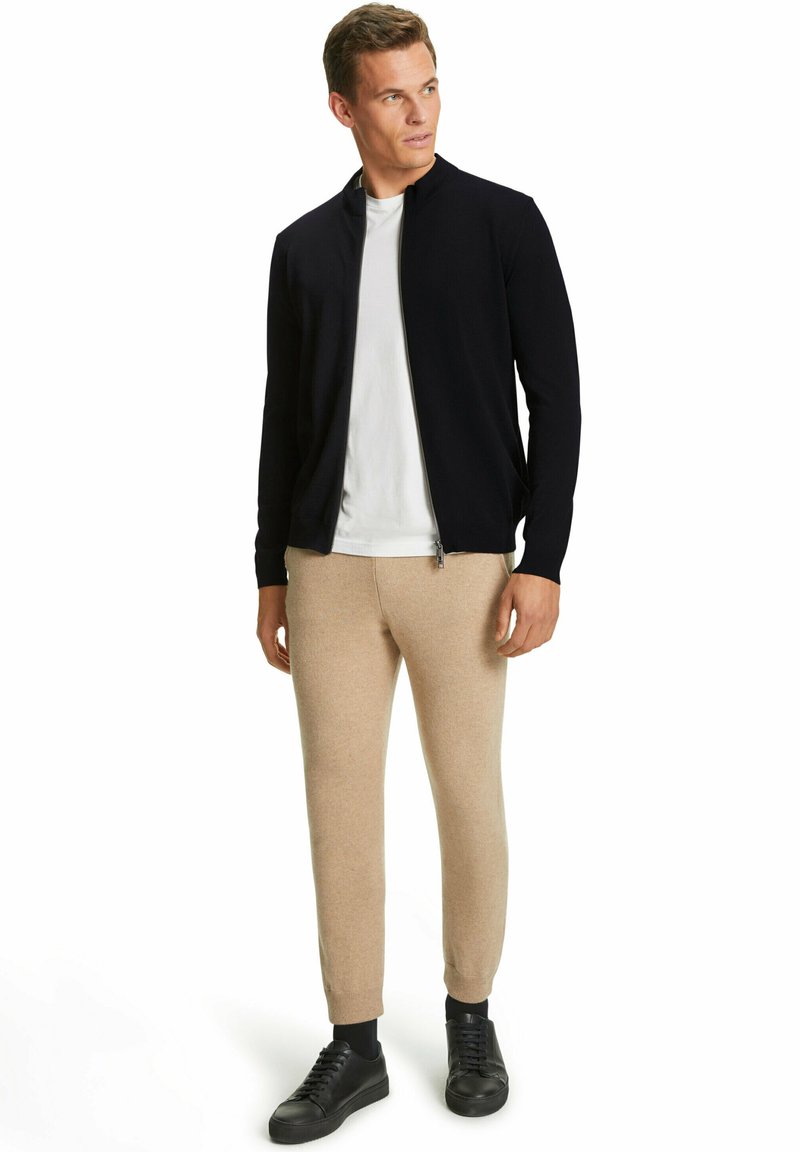 Marineblauer Reißverschlussjacke, weißem T-Shirt, beigefarbenen tapered Pants und schwarzen Sneakers; weicher Stoff mit lässiger Passform. Minimalistisches Design, keine Muster.