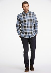 Camisa de cuadros de botón en azul, verde y blanco; de mangas largas; botones marrones; combinada con pantalones oscuros y zapatos marrones.