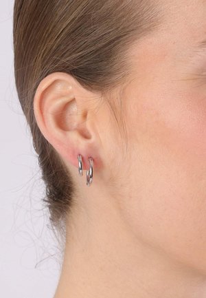 Silver hoop earrings with a polished finish, featuring a circular design and worn in a pierced ear, complementing a neutral skin tone.