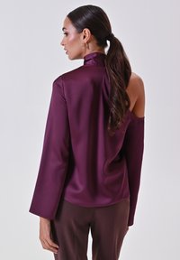 Blusa bordeaux con maniche lunghe e collo alla francese. Presenta un design con spalle scoperte e una texture di tessuto liscia e lucida.