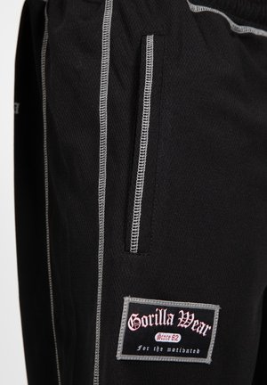 Zwarte sportbroek van een gestructureerde stof, met zilveren stiksel, een zijzak en een opvallende 'Gorilla Wear' logo patch op de dij.