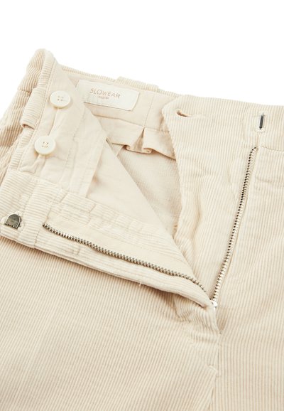 Beige corduroy broek met een rits en knoopsluiting. Kenmerkt zich door een gladde textuur en fijne verticale ribbels. Etiket zegt "SLOWEAR INCOTEX."