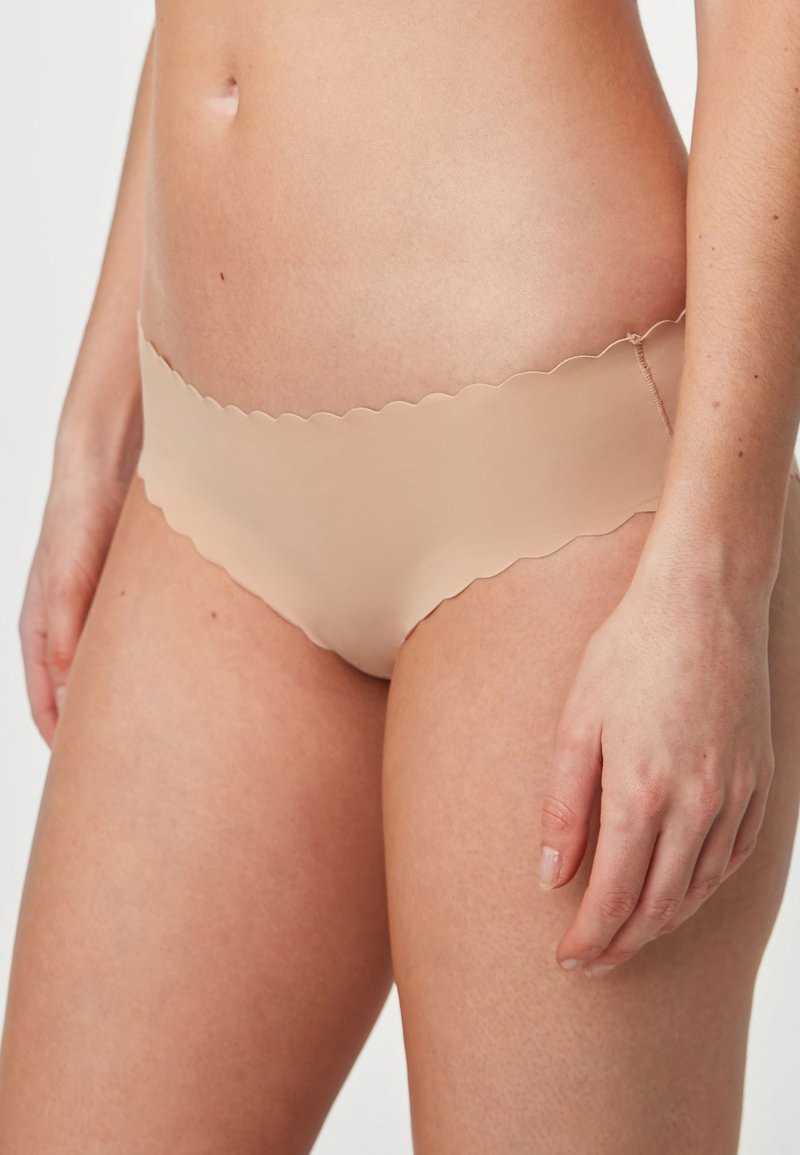 Nude brezšivne hlačke z valovitim pasom, mehko teksturo in minimalno pokritostjo, zasnovane za udobje in gladko prileganje.