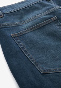 Dunkelblaue Denim-Jeans mit einer Gesäßtasche und kontrastierendem orangefarbenem Stich, einer glatten Textur und einem klassischen Schnitt.