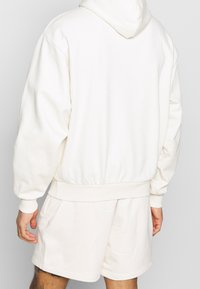 Sudadera blanca con un corte relajado, puños y cintura acanalados. Tejido suave, con capucha fija y detalles de costura sutiles.