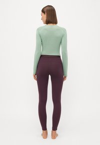 Langermet, lys grønn topp kombinert med mørke lilla tights. Stoffet virker glatt, med en tettsittende design og en enkel snitt.