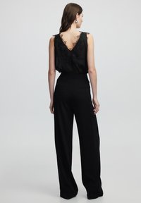Top negro sin mangas con detalles de encaje en la parte de atrás y escote en V profundo, combinado con pantalones de pierna ancha negros de cintura alta.