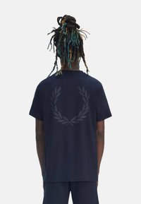Camiseta de algodón azul marino con un gráfico de logo oscuro centrado en un diseño de hoja de laurel en la parte posterior. Mangas cortas y un corte relajado.