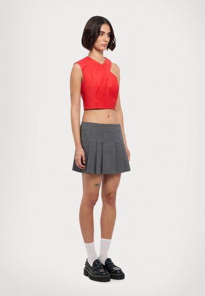 Κόκκινο cropped top με διαγώνια σχεδίαση, συνδυασμένο με γκρι καρό πλισέ φούστα. Το μοντέλο φοράει λευκές κάλτσες και μαύρες πλατφόρμες.