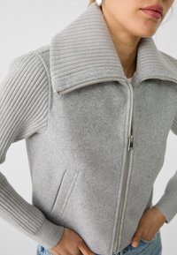 Gray zip-up jacket with ribbed sleeves and a wide collar, made of soft wool-like material; features side pockets and silver zipper hardware.