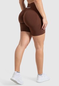 Bruna hög midja shorts i stretchmaterial, med en mjuk textur och en tight passform, kombinerat med vita träningsskor.