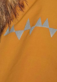 Orange tyg har en texturerad yta med en pälsdetalj. Silvriga triangelmönster syns, vilket kontrasterar mot den livliga bakgrunden.