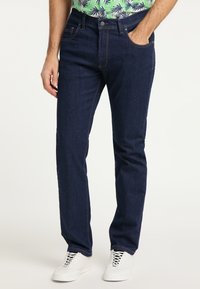 Granatowe dżinsy o prostym kroju, z pomarańczowymi przeszyciami, pięcioma kieszeniami i zapięciem na guzik. Uzupełnione białymi trampkami.