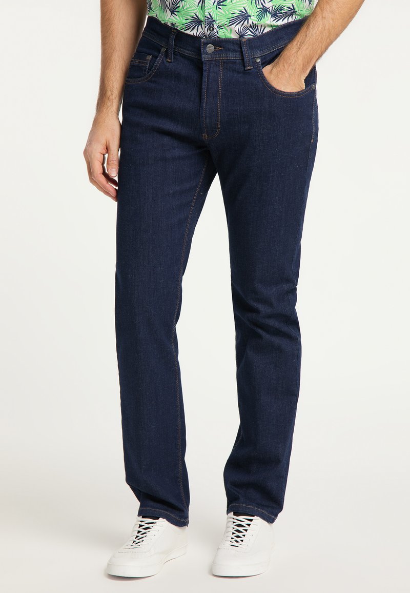 Granatowe dżinsy o prostym kroju, z pomarańczowymi przeszyciami, pięcioma kieszeniami i zapięciem na guzik. Uzupełnione białymi trampkami.