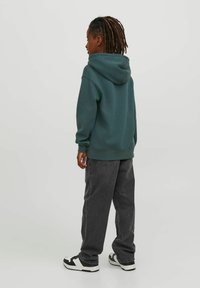 Felpa con cappuccio verde scuro con polsini a coste, abbinata a jeans scuri grigi dalla vestibilità ampia e sneakers bianco e nere.