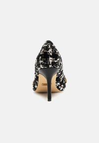 Décolleté alto in tweed bianco e nero con punta affilata e tacco a stiletto sottile. Accento in metallo dorato sul lato. Finitura in tessuto strutturato.