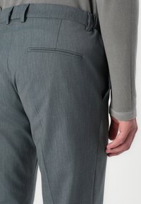 Grijze op maat gemaakte broek met een fijne verticale streeppatroon, voorzien van een achterzak en tapered pijpen. De tailleband is plat met riemlussen.