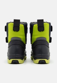 Schwarze und limegrüne wasserdichte Stiefel mit einer strukturierten Oberfläche, verstärktem Absatz und verstellbaren Riemen; innen mit Kunstfell gefüttert; robuste Sohle.