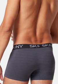 Gråstribede boxershorts med sort elastik i taljen, der har mærkenavnet "SKINY" i hvid skrift, lavet af et glat stof.