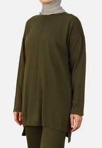 Olive green long-sleeve tunic, made of textured fabric, features a round neckline, side slits, and a relaxed fit.