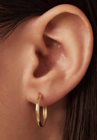 Gouden oorring in de oorlel, met een gladde, glanzende oppervlakte en een subtiele textuur. Close-up van het oor.