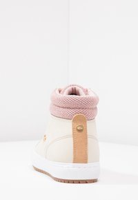 Zapatilla crema con puño de punto rosa, material de ante, acento en cuero marrón claro en el talón, suela blanca y detalle del logo en dorado.
