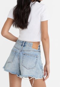 Top corto de manga corta blanco combinado con pantalones cortos de mezclilla de talle alto en azul claro, con bordes deshilachados y una etiqueta de cuero cosida en la cinturilla.